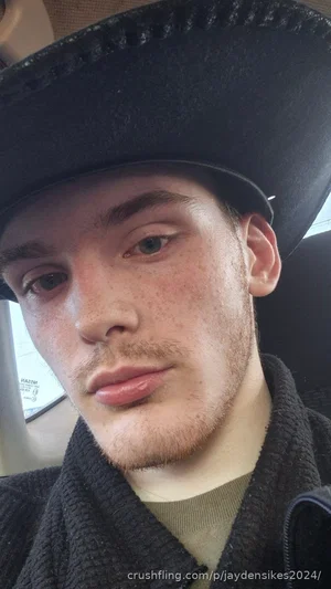 man with freckles wearing black hat and dark jacket, sitting in a car