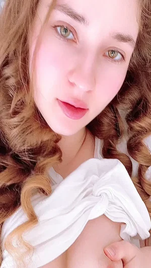 Woman with curly hair in white top, close-up selfie indoors.