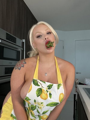 Blonde woman in lemon apron posing in kitchen.
