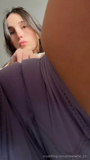 Woman with dark hair and silver streaks in a purple top, posing indoors with hand under chin.