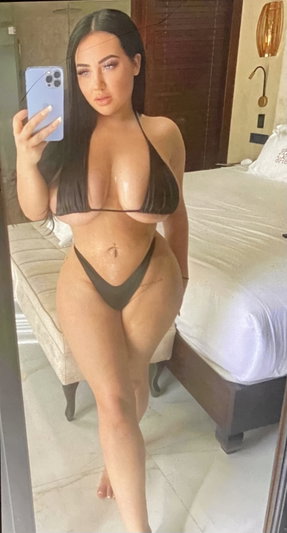 Curvy woman in black bikini taking mirror selfie in bedroom.
