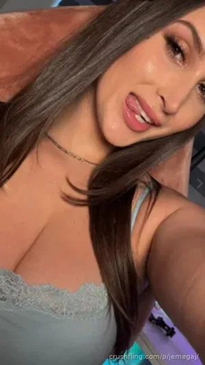 Woman with long brown hair in light blue lace top, smiling in close-up selfie.