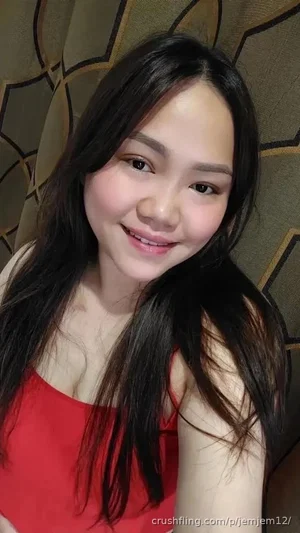 Woman with long dark hair in red top, smiling, indoors near patterned curtain.