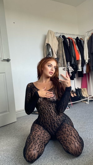 Curvy redhead in black lace bodysuit kneels by wardrobe.
