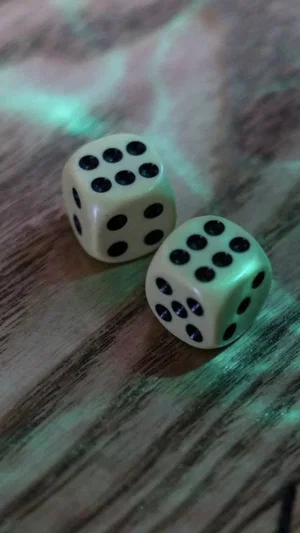 Two white dice with black dots on a wooden surface under green lighting.