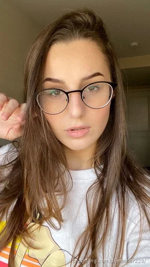 Woman with long brown hair and glasses wearing a white graphic tee, indoors.