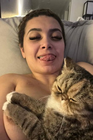 Brunette woman topless holding cat on couch.