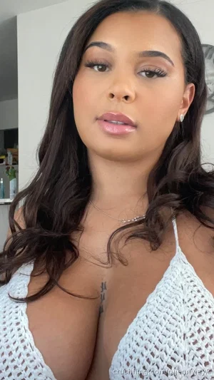 Woman with long dark hair in white crochet top, indoor setting.