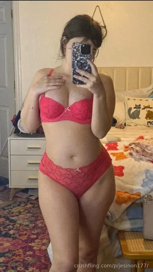 Woman in red lace lingerie taking mirror selfie in bedroom.