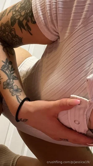 Woman with tattoos in pink ribbed top and white shorts, holding waist indoors.