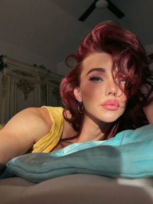 Red-haired woman in yellow top lying on bed.