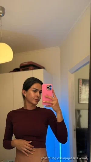 Woman in maroon long-sleeve crop top taking mirror selfie in indoor setting.