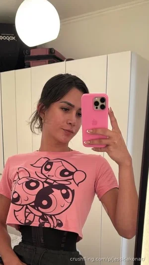 Woman in pink crop tee with cartoon print, black corset, holding pink phone for mirror selfie in