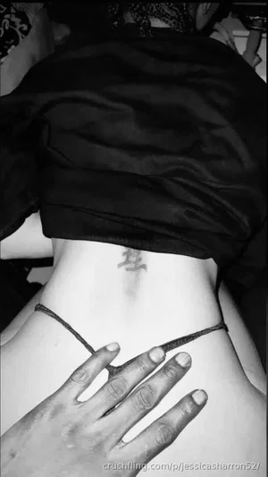 Woman with tattoo on lower back, wearing black top, hand on hip, indoor setting.