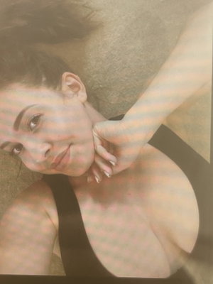 Woman with short hair lying down, wearing black top, hand near neck, soft lighting.