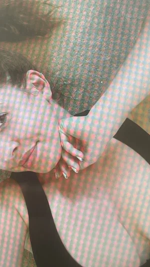 Woman with dark hair lying down, wearing black top, hand near face, checkered overlay.