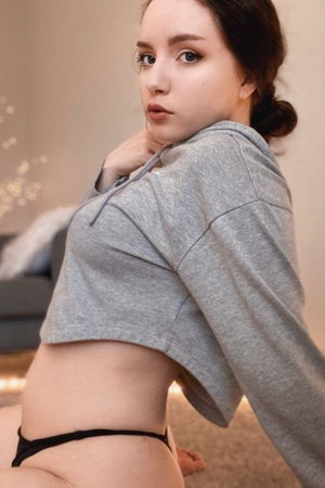 Woman in grey crop hoodie and black underwear posing indoors.