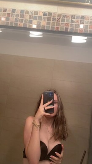 Woman with long hair taking bathroom mirror selfie in black bra.