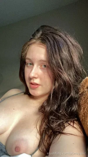Woman with long dark hair, bare chest, thin strap visible, indoors.