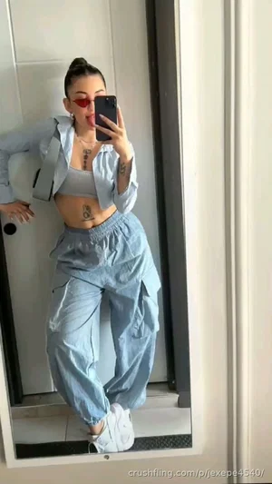 Woman in light blue outfit takes mirror selfie, wearing crop top, jacket, baggy pants, white
