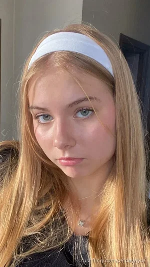 Blonde woman with white headband, wearing black top, indoors.