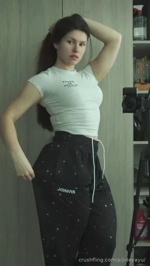 Woman in white crop top and black star-patterned pants posing indoors against a wall.