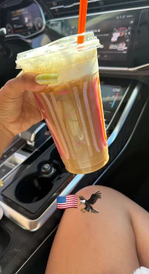 Person holding iced drink in car, thigh visible with eagle and flag tattoos.
