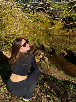 Woman in black activewear squatting by a stream outdoors.