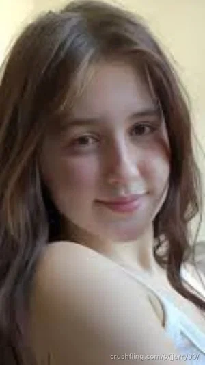 Woman with long brown hair in a light top, indoor setting, smiling at camera.