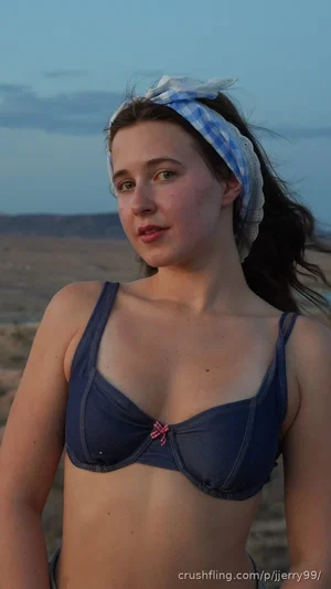 Woman in blue bikini top and checkered headband on beach at dusk.