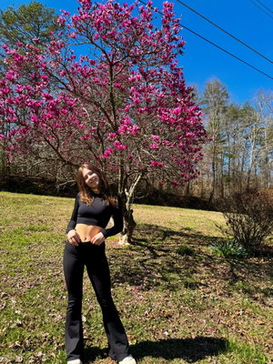 Woman in black crop top and pants outdoors by flowering tree.
