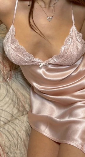 Woman in pink lace bra and satin slip, lying on patterned bedding.