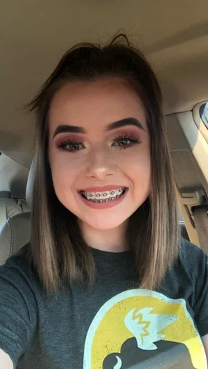 Woman with brown hair and makeup, wearing a graphic t-shirt, taking a selfie in a car.