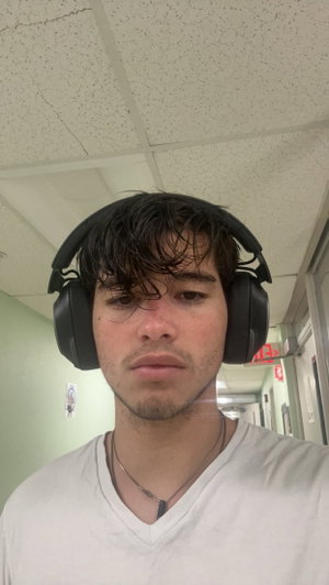 Man with dark hair wearing headphones and white t-shirt in hallway.