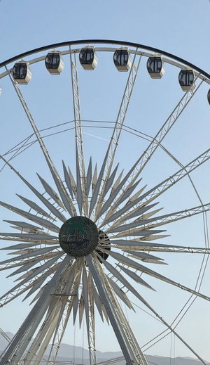 Ferris wheel with central logo against clear blue sky.