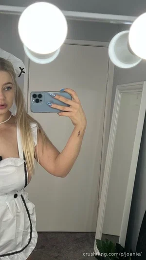 Woman in white sailor outfit with blonde hair taking mirror selfie indoors.
