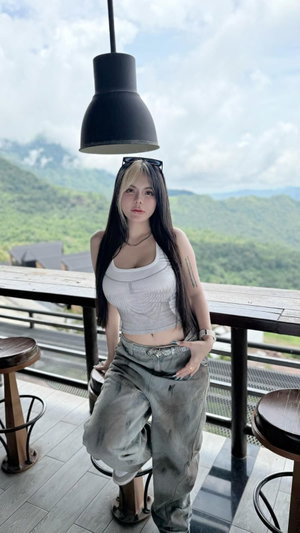Long-haired woman in white crop top and grey pants on outdoor balcony.