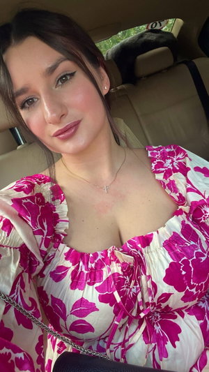 Brunette woman in floral top taking car selfie.