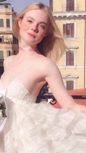Blonde woman in white ruffled dress posing outdoors with buildings in background.