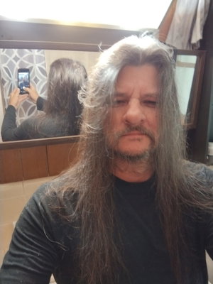 Man with long gray hair and beard wearing black shirt, taking mirror selfie in bathroom.