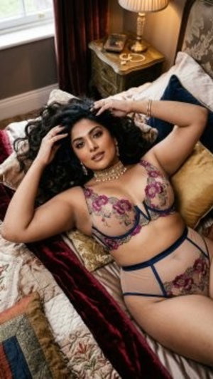 Woman with dark curly hair in floral lingerie lying on bed in bedroom.