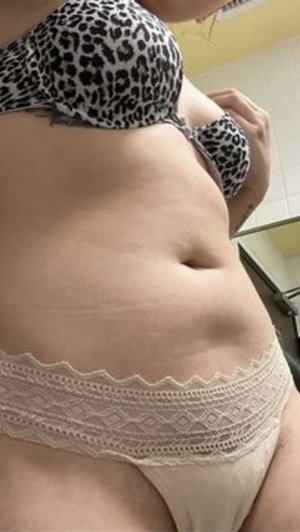 Woman in leopard print bra and lace underwear, showing midriff in indoor setting.