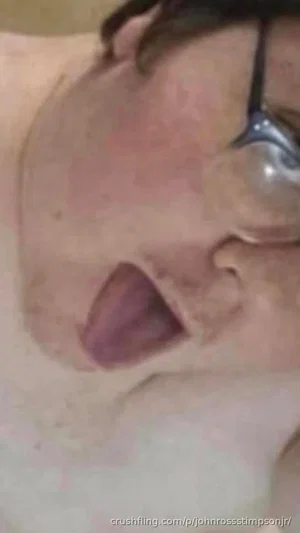 Close-up of a person with dark hair and glasses, mouth open, skin visible.