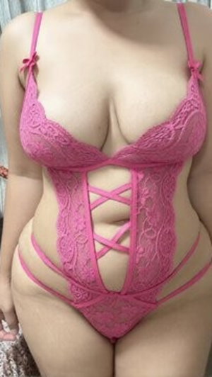 Woman in pink lace lingerie posing indoors, curvy body type.