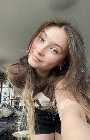Woman with long brown hair taking indoor selfie in t-shirt.