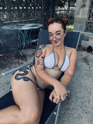 Woman with tattoos in white bikini top sitting on lounge chair outdoors.