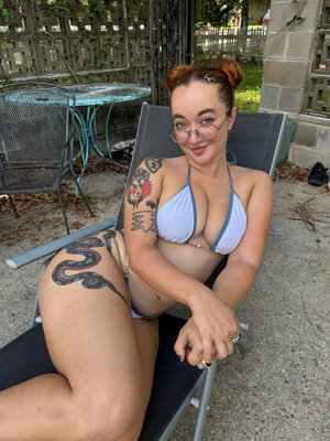 Curvy woman with red hair and tattoos wearing bikini outdoors.