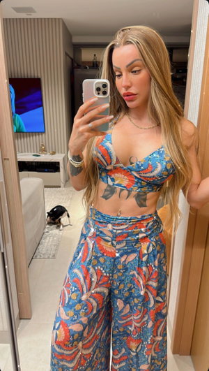 Curvy blonde in colorful bikini top and pants, bedroom mirror selfie.