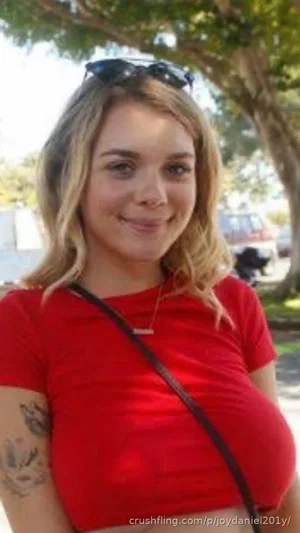 Woman with blonde hair in red crop top, tattoo on arm, outdoors near trees.