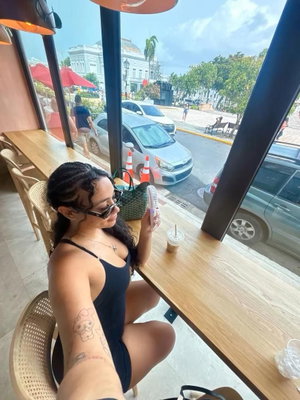 Woman in black bodysuit taking selfie in cafe by window.
